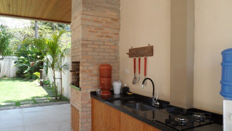 Área com churrasqueira, cooktop, pia e mesas. 