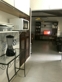 Vista da cozinha e ao fundo a sala com TV a cabo e ar-condicionado.