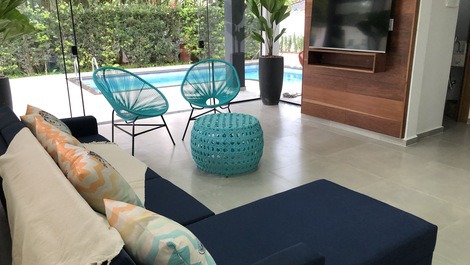 Sala de estar com vista à piscina e paisagismo. sofá confortável e tv  de 50 polegadas com sky.