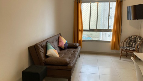 Vista da sala com sofá cama, smartv, mesa com cadeiras e a janela com rede de proteção 