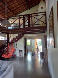 Foto da entrada. 1° piso: sala, quarto e banheiro ao fundo, balcão americano a direita e porta dos fundos com saida para varanda e quintal. 2° piso: mezanino com porta para quarto com suite.