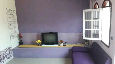 Sala com tv, sofá cama de casal, sofá de 2 lugares e um ventilador