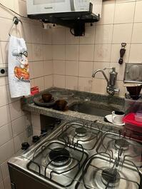 Cozinha: microondas no suporte, pia com  torneira filtro, utensílios de cozinha( panelas, pratos, talheres) e fogão com 4 bocas 