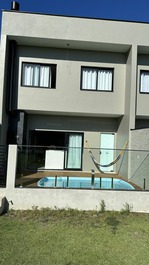 Fundos deck com piscina, churrasqueira, lavanderia/chuveiro e portão de acesso ao gramado.