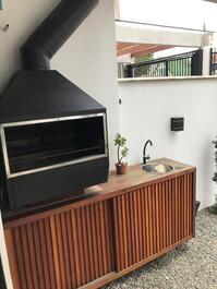 Churrasqueira suspensa com armário e pia na área da garagem coberta com um espaço com deck com móveis.