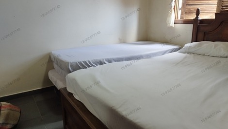 Quarto principal com ar condicionado cama de casal com uma cama de sobressalente ao lado com roupas 