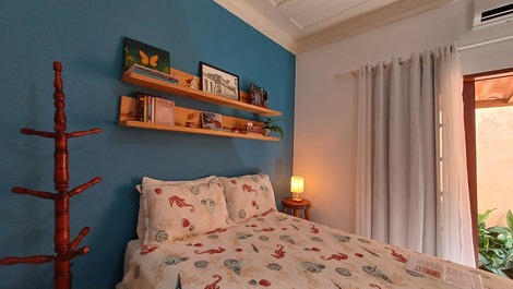 Cama, estante de livros, cabideiro, luminária de luz amarela, cortina e entrada do quarto