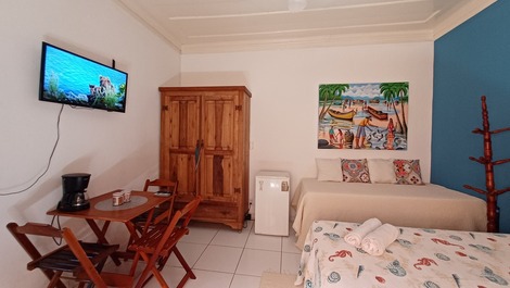 Panorâmica do quarto, incluindo camas, frigobar, armário, tv, mesas, cadeiras e entrada do banheiro