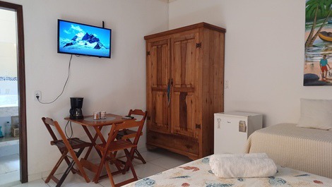 Foco no frigobar, armário, tv, mesas, cadeiras e entrada do banheiro