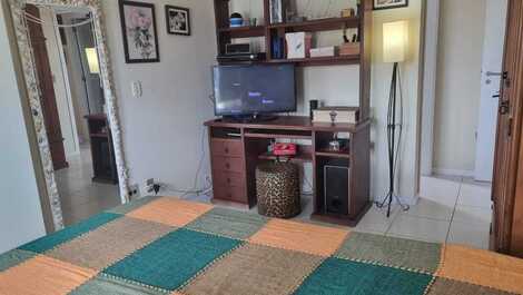 Vista contrário da suíte com porta do banheiro ao fundo , móvel com mesa de trabalho e tv.